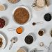 Flat lay of various dried grains, seeds, and beans arranged in bowls and measuring cups on marble.